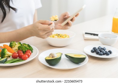 Dieting Asian Young Woman Eating Keto Food, Hand Holding Spoon Eating Egg Salad In Bowl, Diet Plan Nutrition With Vegetables While Using Smartphone. Nutritionist Of Healthy, Nutrition Of Weight Loss.