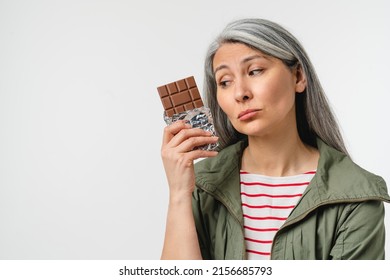 Dieting, Gaining Weight With Calories. Unhealthy Junk Food. Mature Middle-aged Woman Eating Chocolate Bar Isolated In White Background. Acne, Climax, Menopause