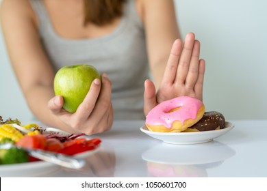 Dieting or good health concept. Young woman rejecting Junk food or unhealthy food such as donut or dessert and choosing healthy food such as fresh fruit or vegetable. - Shutterstock ID 1050601700