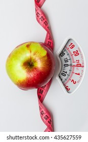 Dieting Healthy Eating Slim Down Concept. Closeup Apple With Measuring Tape On White Weight Scale