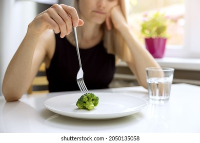 dieting problems, eating disorder - unhappy woman looking at small broccoli portion on the plate - Shutterstock ID 2050135058