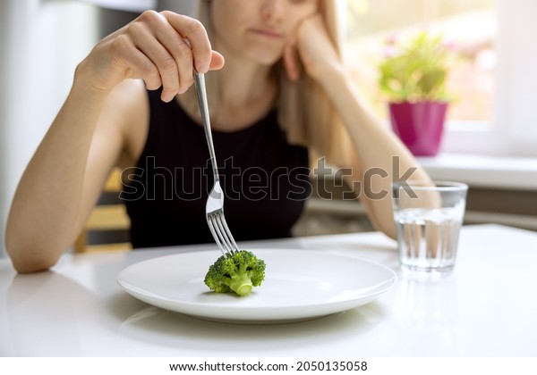 dieting problems, eating disorder -\
unhappy woman looking at small broccoli portion on the\
plate