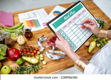Dietitian writing a diet plan, view from above on the table with different healthy products and drawings on the topic of healthy eating - Shutterstock ID 1288986586