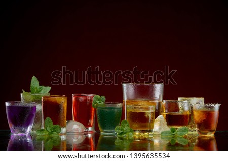 Different alcoholic drinks in clear glasses with ice and mint on red background
