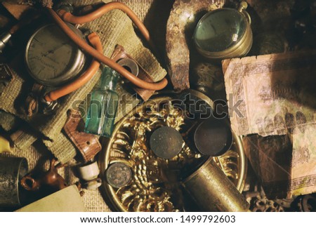 Different antique items on the table: bronze jewelry, old money, retro manometer, magnifier, glass bottle, silverware. Vintage background from a collection of antiques. Close-up selected focus