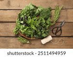 Different aromatic herbs in wicker basket, thread and scissors on wooden table, flat lay