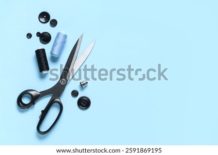 Different black buttons with thread spools and scissors on blue background