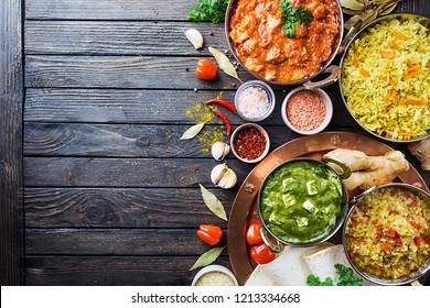 Different bowls with assorted indian food on dark wooden background, top view. Dishes and appetizers of indian cuisine. Chicken, curry rice, lentils, paneer, chapati and spices.