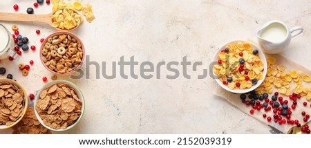 Different breakfast cereals, milk and berries on light background with space for text