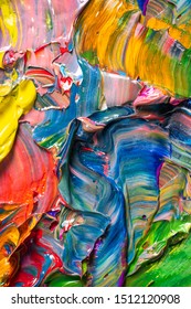 Different bright colors of oil paints are mixed on a palette close-up.