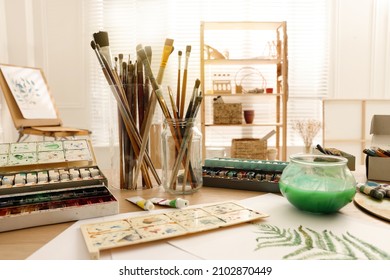Different brushes and paints on wooden table in studio. Artist's workplace