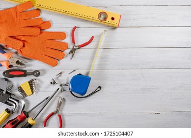 Different building or crafting tools and gloves flatlay on white wooden background