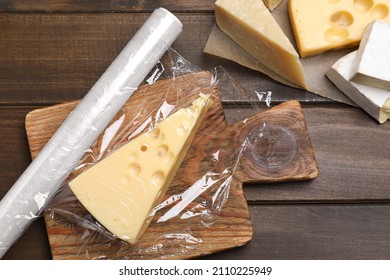 Different Cheeses And Plastic Food Wrap On Wooden Table, Flat Lay