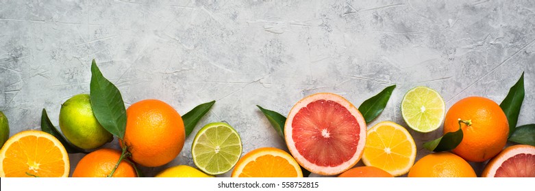 Different citrus fruit on grey concrete table. Whole and sliced fruit. Food background. Healthy eating and diet. Long banner format good for web.