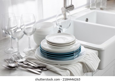 Different clean dishware, cutlery and glasses on countertop near sink in kitchen