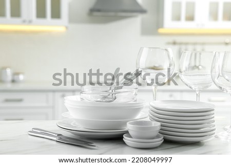 Different clean dishware, cutlery and glasses on white marble table in kitchen