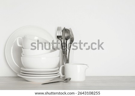 Different clean dishware on light wooden table near white wall, space for text