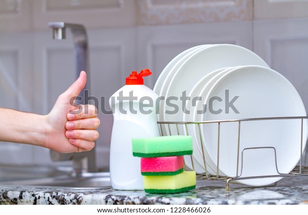 Different clean plates in dish drying rack, dish sponges\
and dishwashing detergent on the table on kitchen counter. Clean\
dishes 