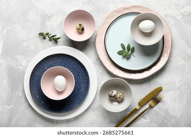 Different clean plates with Easter eggs and fresh green leaves on grey background