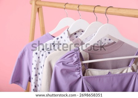 Different clothes hanging on rack against pink background, closeup