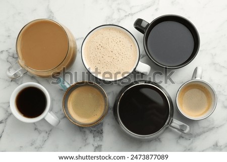 Different coffee drinks in cups on white marble table, flat lay