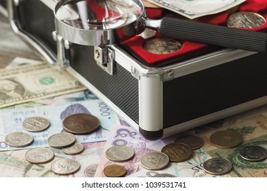 Different collector's coins and banknotes in the box with a magnifying glass, soft focus background