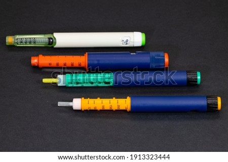Different colored insulin syringe pens for diabetes treatment on black background. Insulin injection pen for hormone therapy