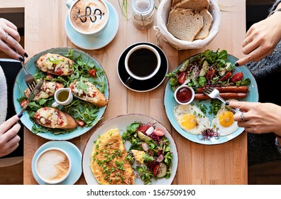 Different Colorful Meals For Breakfast Or Lunch Time On A Plate With Cutlery On Woman's Hands. Fried Eggs, Omelette, Bruschetta And Sausage On A Wooden Teble In Restaurant. Flat Lay Top View.