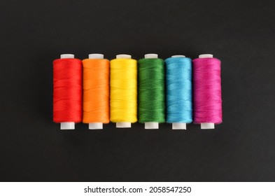 Different colorful sewing threads on black background, flat lay
