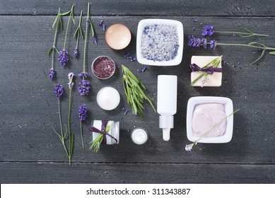 Different Cosmetic Creams, Bath Salt, Soap, Anti Aging Serum Pipette With Fresh Lavender Flowers On Black Wooden Texture