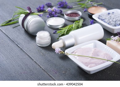 Different Cosmetic Creams, Bath Salt, Soap, Anti Aging Serum Pipette With Fresh Lavender Flowers On Black Wooden Texture