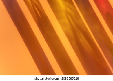 Different cosmetic glass bottles standing on orange beige background. Abstract pattern by shadows and illuminating reflections in the sunlight. Red and yellow shades. Flat lay style with copy space