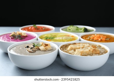 Different cream soups and tasty broth in bowls on gray table, closeup - Shutterstock ID 2395421825