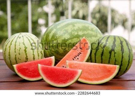 Different cut and whole ripe watermelons on wooden table outdoors