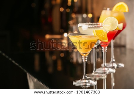 Different delicious cocktails on black table in bar. Space for text