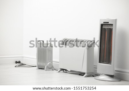 Different electric heaters near white wall indoors