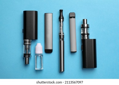 Different electronic cigarettes and liquid solution on light blue background, flat lay