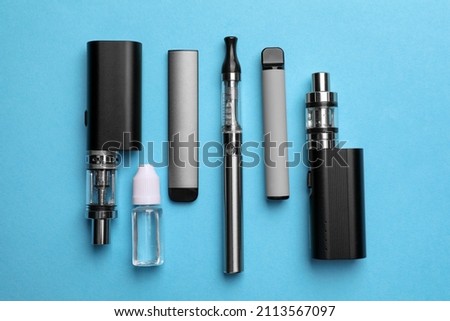 Different electronic cigarettes and liquid solution on light blue background, flat lay