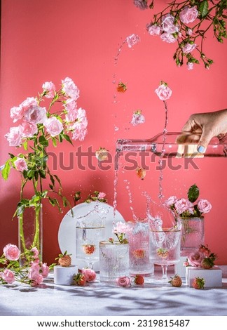 Different elegant glasses with sparkling wine, pink roses and strawberry, women hand is pouring wine from bottle to glass. Splash, splatter, fly rose flowers and white strawberry pineberry