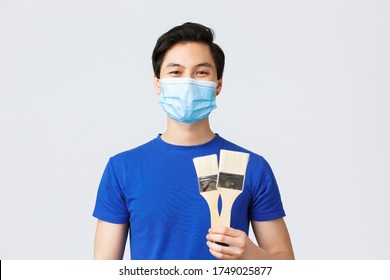 Different Emotions, Lifestyle And Leisure During Coronavirus, Covid-19 Concept. Time To Renovate Our House. Cheerful Smiling Asian Man Holding To Painting Brushes, Repair Home During Self-quarantine