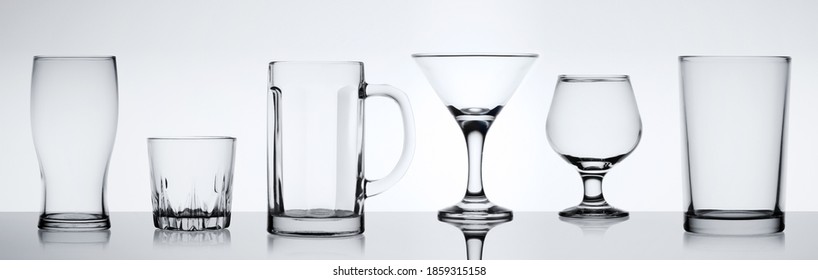 Different empty glasses for alcoholic drinks on a white background. Collectible set of glassware on glossy table surface.