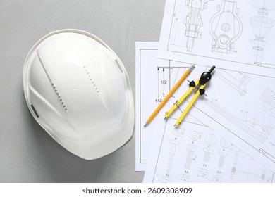 Different engineering drawings, hard hat, pencil and divider on grey table, flat lay