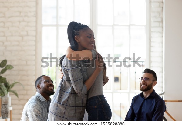 Different ethnicity people gathered together in\
rehab center try overcome addiction or mental problems, african\
woman psychologist counsellor hugging girl supporting her, group\
therapy session\
concept