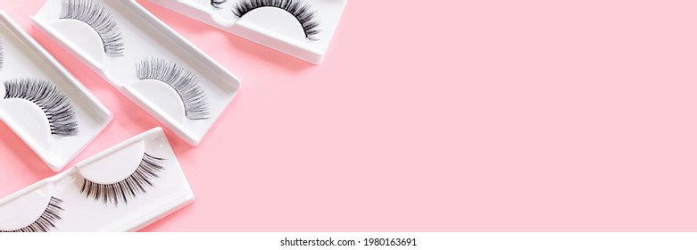 Different fake eyelashes on trendy pastel pink background. Beauty pattern. Makeup accessories. Cosmetics products for women. Top view, flat lay. Layout. Copy space. Place for text and design. Banner.