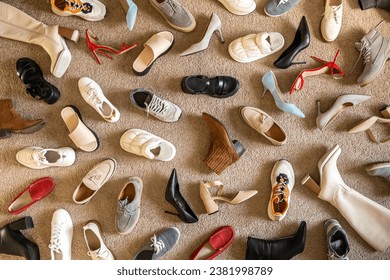 Different female shoes abstract arrangement on beige carpet flooring fashion shopping background. Woman femininity footwear random lying on floor unreasonable consumption vogue trendy backdrop