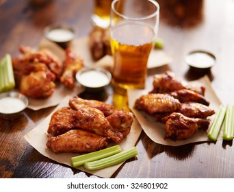 different flavored chicken wings on wax paper served with beer, ranch dressing and celery sticks