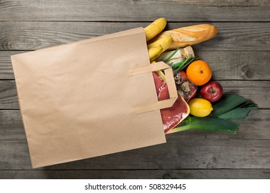 Different food in paper bag on wooden background, close up. Grocery shopping concept, top view