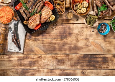 Different foods cooked on the grill on the wooden table with copy space, grilled steak, grilled sausage and grilled vegetables. Top view - Powered by Shutterstock