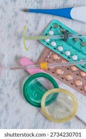 Different forms of birth control are arranged on a flat surface. Items include pills, condoms, a syringe, and a device used to prevent pregnancy.