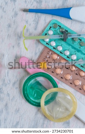 Different forms of birth control are arranged on a flat surface. Items include pills, condoms, a syringe, and a device used to prevent pregnancy.